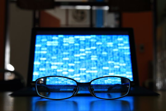Glasses in front of laptop monitor. digital screen displayed blue light code blocks. computer language coding development concept. back of the house big data work environment. 