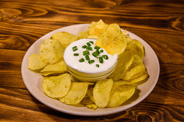 Ceramic plate with potato chips and glass bowl with sour cream on wooden table