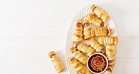 Scary sausage mummies in dough with funny eyes on table.  Halloween food. Top view. Flat lay. Banner