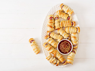 Scary sausage mummies in dough with funny eyes on table.  Halloween food. Top view. Flat lay. Banner