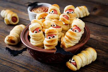 Scary sausage mummies in dough with funny eyes on table.  Halloween food. Top view. Flat lay. Banner - Powered by Adobe