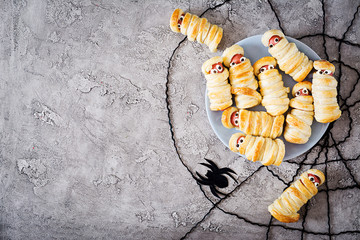 Scary sausage mummies in dough with funny eyes on table.  Halloween food. Top view. Flat lay. Banner