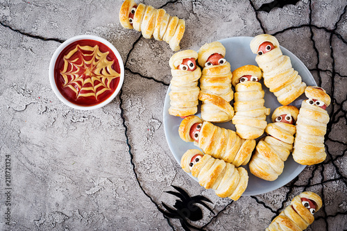 Scary sausage mummies in dough with funny eyes on table.  Halloween food. Top view. Flat lay. Banner