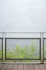 Expanded metal balcony rail with white wall and green tree background and wooden deck floor