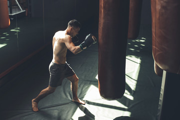 Top view of shredded topless man boxing with punching bag. He is having hard cardio workout with...