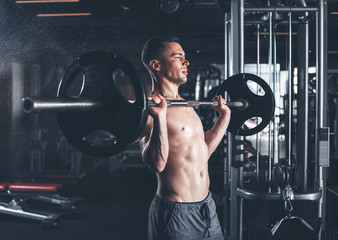 Sportsman is standing and lifting barbell. He is doing shoulder press during strength workout in sport club. Training with weight concept