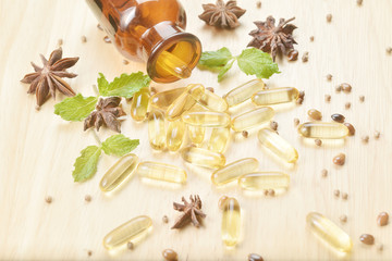 Fish oil capsules with omega 3 and vitamin D spread out of a  brown glass bottle on wooden texture, healthy diet concept.