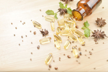 Fototapeta na wymiar Fish oil capsules with omega 3 and vitamin D spread out of a brown glass bottle on wooden texture, healthy diet concept.