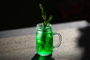 Closeup jar of green cucumber and tarragon lemonade at table background.