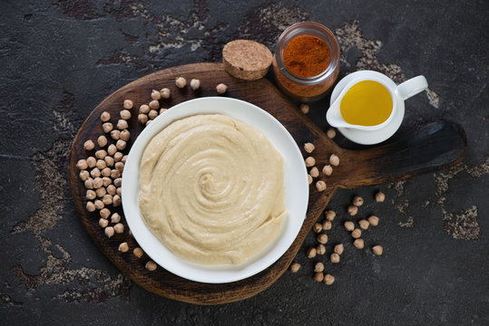 Above view of creamy hummus with raw chickpeas, paprika and olive oil over brown stone background, horizontal shot