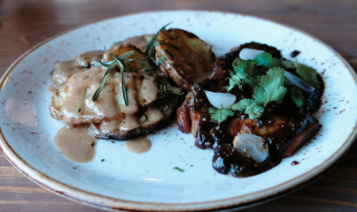Piece of pork cooked on the coals with potatoes, gravy and greens on plate, top view.