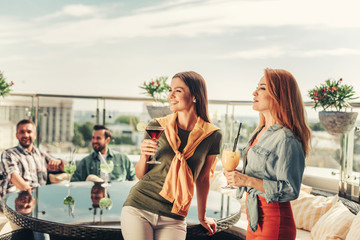 Best friends. Smiling lovely women enjoying drinks at rooftop bar. Bearded man sitting at the table...