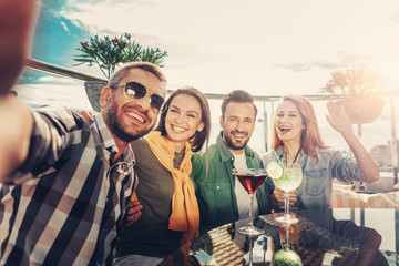 Nice shot. Group of cheerful friends taking photo while sitting at the table with cocktails - Powered by Adobe