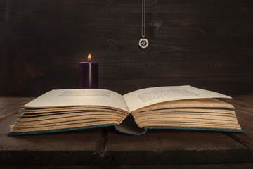 An open old book on a dark background with a burning candle, a pentacle, and copy space