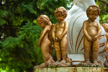 Fototapeta na wymiar Close-up of three little angel boys statues, covered with bronze stand on a fountain in the city park