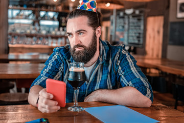 Beer on birthday. Bearded dark-haired man feeling not very cheerful while drinking some beer on his birthday