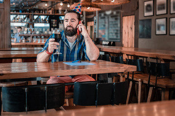 Beer in pub. Dark-haired man wearing blue squared shirt and bright red trousers drinking beer in pub