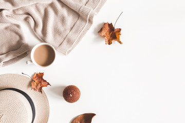 Autumn composition. Cup of coffee, hat, dried autumn leaves, beige sweater on white background....