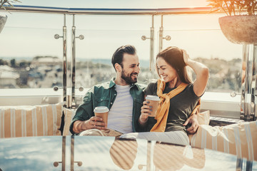 We are in love. Happy bearded man looking at pretty young lady while hugging her. They are holding cups of coffee and smiling