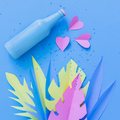 Painted in deep blue beer or cocktail bottle lies among hearts and palm tropical leaves made of paper. Summer vacation party concept