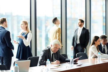 Senior businessman making notes while sitting by table in working environment in conference hall