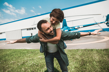 Portrait of satisfied child embracing beaming bearded daddy while having fun with him outside...