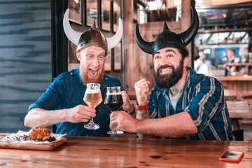 Clanging glasses. Two mature men feeling extremely entertained while clanging their glasses with beer sitting in the pub