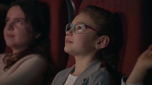Beautiful girl in glasses watching cartoon film at movie theater. Girl smiling in movie theatre. Cinema kids concept. School girl spending time in cinema. Kid watching movie in slow motion