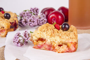 homemade pie with plums decorated with currants, strawberries and flowers on a white wooden table