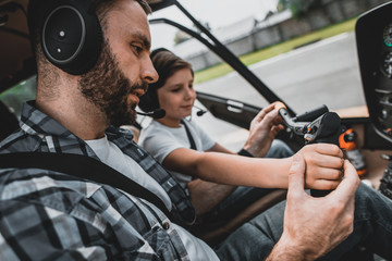 Side view positive bearded man teaching beaming kid to control helicopter. He describing instruction him. They wearing modern earphones