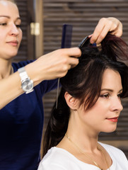 Naklejka premium Hairdresser does hairstyle for luxurious woman. coiffure in the form of big curl. Concept wedding hairstyle