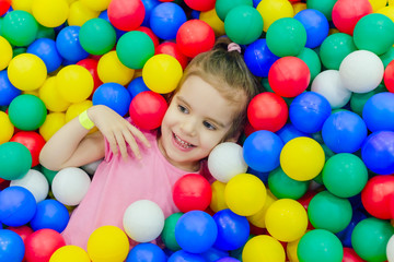happy little girl having fun in ball pit with colorful balls.