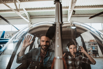 Portrait of beaming bearded father and positive boy gesticulating arms while wearing headsets. They...