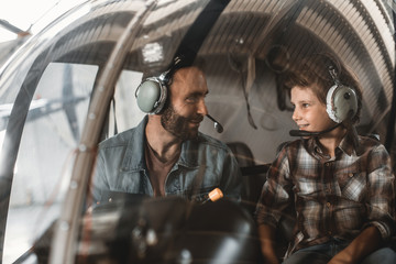 Obraz na płótnie Canvas Side view optimistic bearded male speaking with pleased little boy. They controlling rotor plane while wearing special headsets. Glad father with son spending time together concept