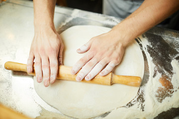 Obraz na płótnie Canvas Overview of baer hands with rolling-pin rolling fresh handmade dough for pizza