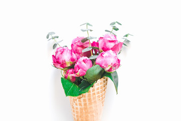 Creative minimalist composition with waffle cone with pink roses and eucalyptus inside on white background. The concept of gift and celebration. Flat lay, top view.