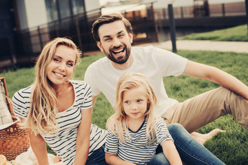 Portrait of cheerful unshaven man and satisfied lady having leisure with smiling child. Positive family relaxing outdoor concept