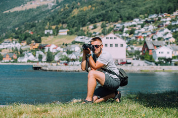 Fototapeta na wymiar Young beard male tourist with photo camera in sportswear spending time enjoying view in coast in Aurland, Norway. Travel professional photography concept.