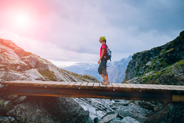 Young woman traveler with backpacker and bandana going on wooden bridge in cliff during trip...