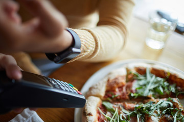 Smartwatch on human hand over payment machine in process of contactless paying in modern cafe