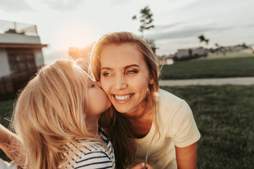 Cheerful kid expressing love for mom. She kissing her in cheek. Positive parent with child outside concept