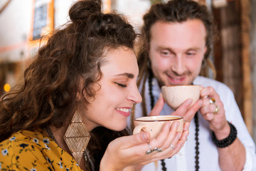 Taste of tea. Curly appealing woman wearing nice stylish earrings smelling taste of nice tea