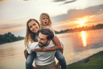 Portrait of smiling bearded dad having fun with outgoing woman and glad little daughter. He talking...