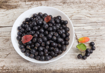 Chokeberry in bowl and berries cluster on old wooden surface