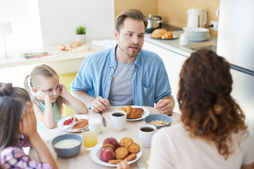 Nervous husband talking to his wife by breakfast with their two little daughters sitting near by