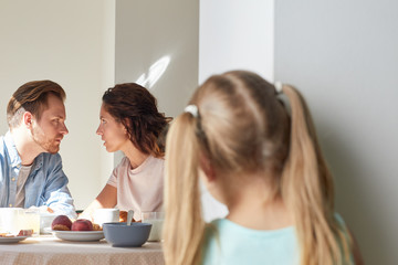 Young man and woman having intimate talk by breakfast while their daughter eavesdropping by kitchen...
