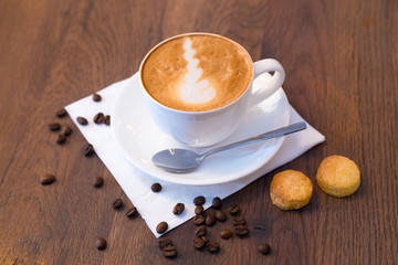 Closeup of a cup of coffee with beans and cookies on dark wooden table