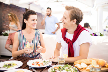 Young cheerful couple sitting by table, enjoying talk and having vegetarian lunch in modern cafe