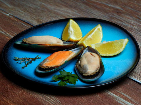 Fresh mussels and quartered lemons set on a blue plate, placed on a dark brown wooden surface