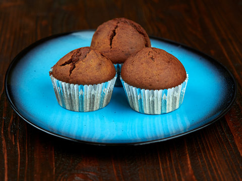 Home baked cocoa muffins set on a bright blue plate, placed on a dark brown wood board